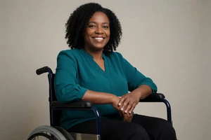 Black woman in a wheelchair smiling in a studio portrait on a wheelchair dating site
